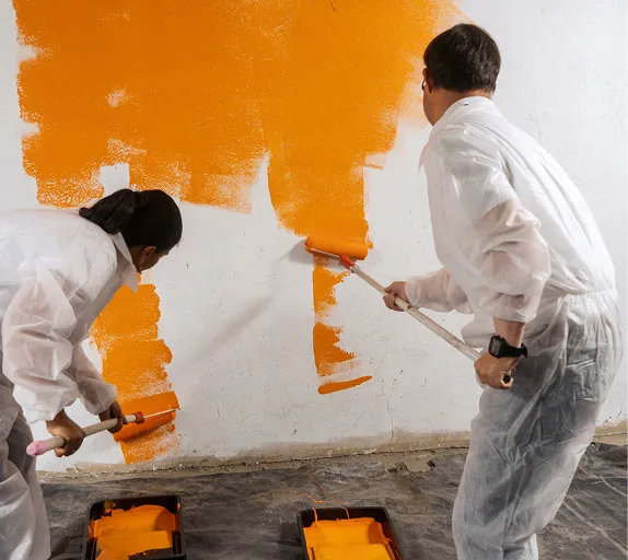 Zwei Maler in Schutzanzügen streichen eine Wand orange